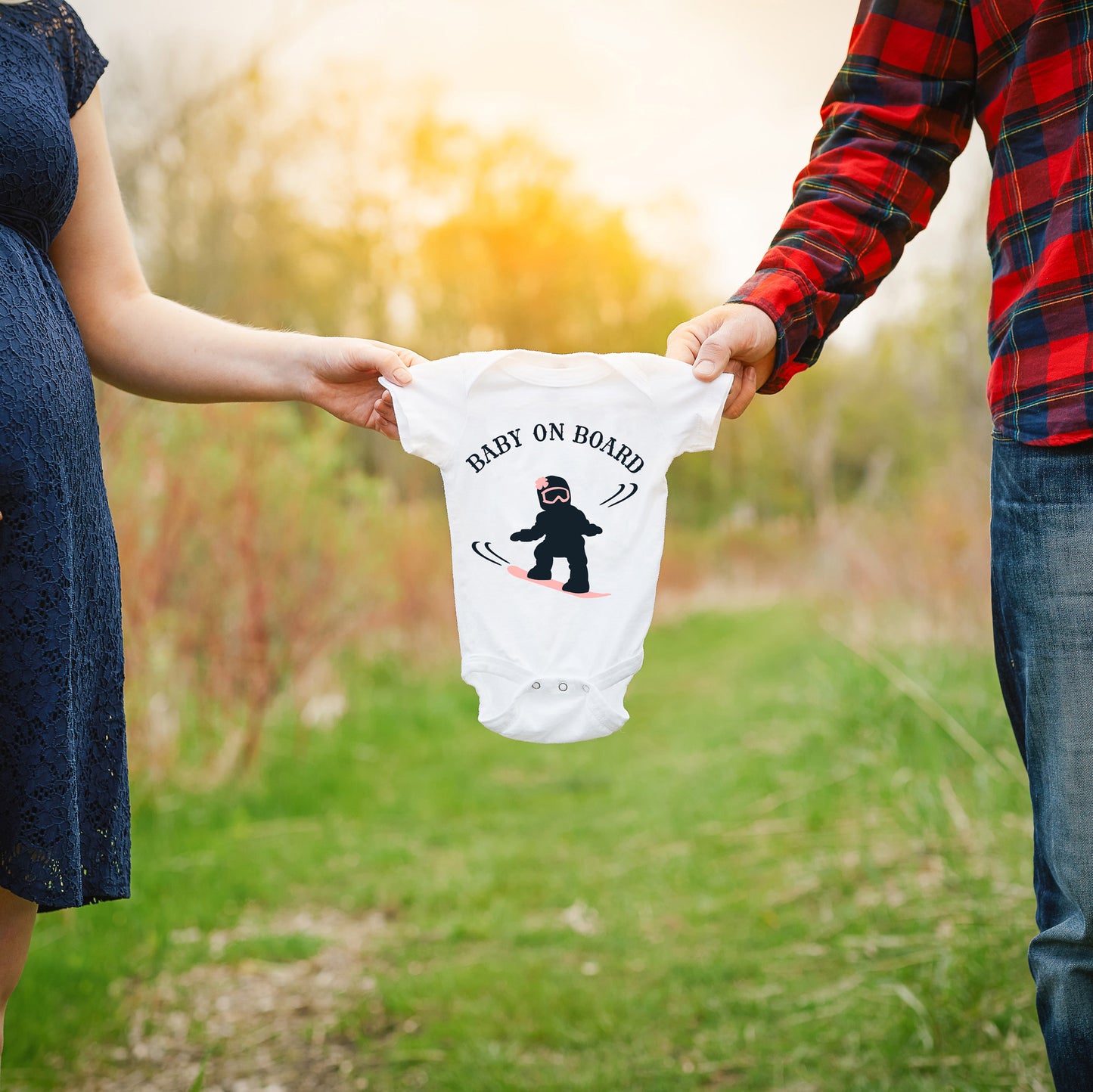 
                  
                    a couple holding a onesie between them with Baby on Board - Snowboarding Girl svg printed on it as a baby announcement
                  
                