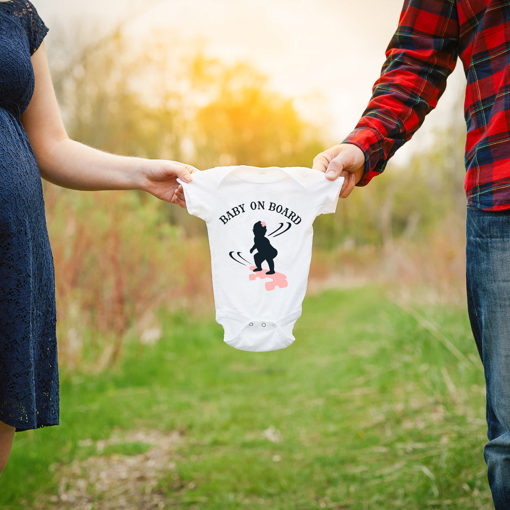 a couple holding a baby onesie between them, printed with Baby On Board - Skateboarding Girl SVG as a pregnancy announcement