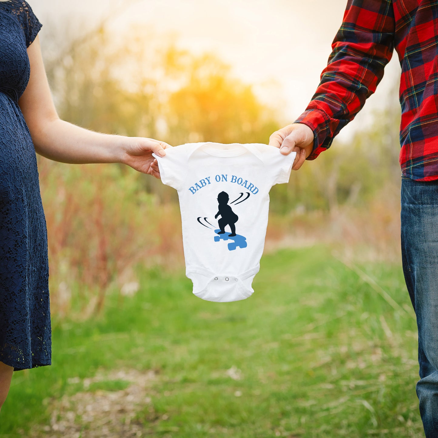 
                  
                    a couple holding up a onesie with baby on board - skateboarding boy svg printed in blue as a gender reveal announcement
                  
                