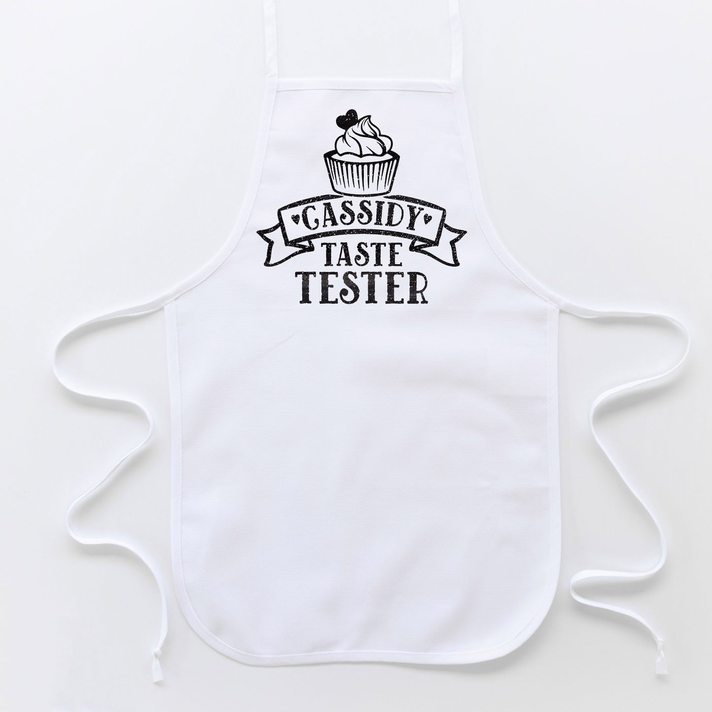 
                  
                    a toddler cupcake taste tester apron in white with black glitter print
                  
                