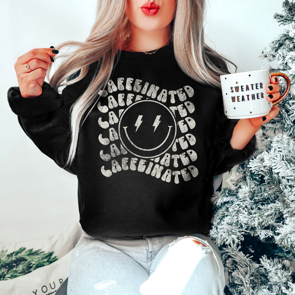a young woman amped up, holding a coffee cup, in a winter scene wearing a caffeinated sweatshirt in black