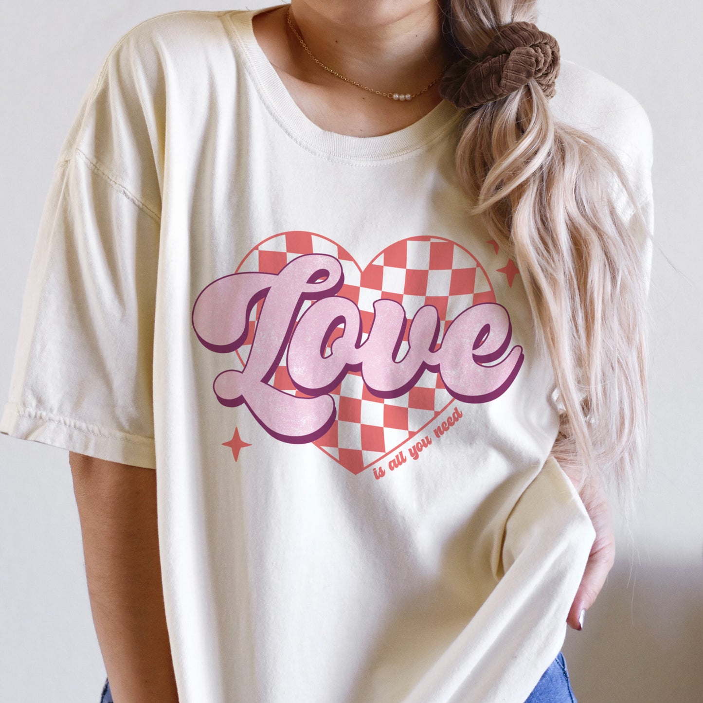 
                  
                    a young woman wearing a retro, love is all you need, comfort colors tee in Ivory
                  
                