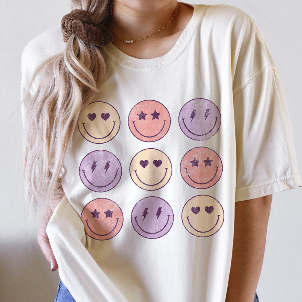 
                  
                    a young woman wearing a smiley face, love tic tac toe shirt in Ivory
                  
                