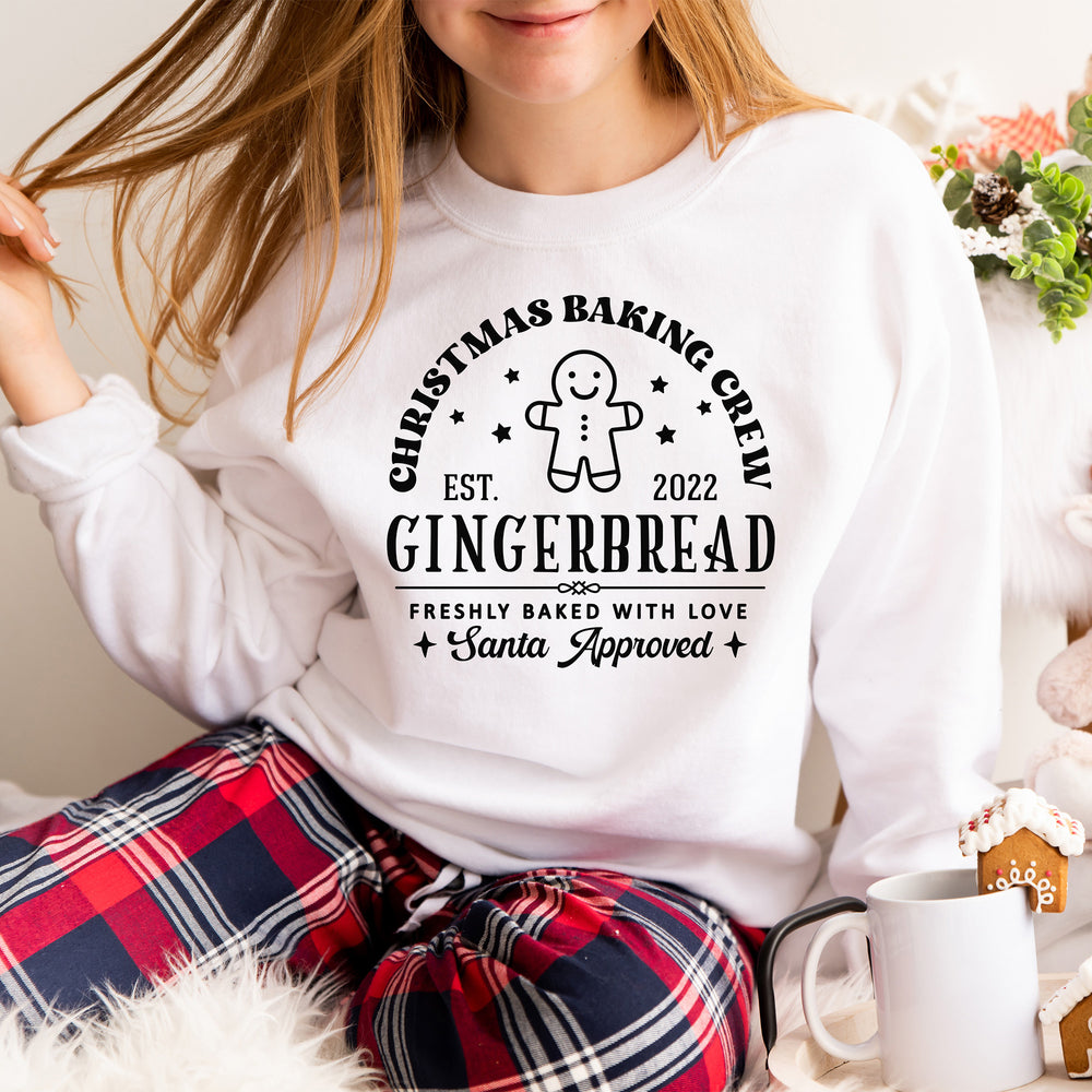 A teenager in a christmas scene, wearing  a customizable christmas baking crew sweatshirt in white