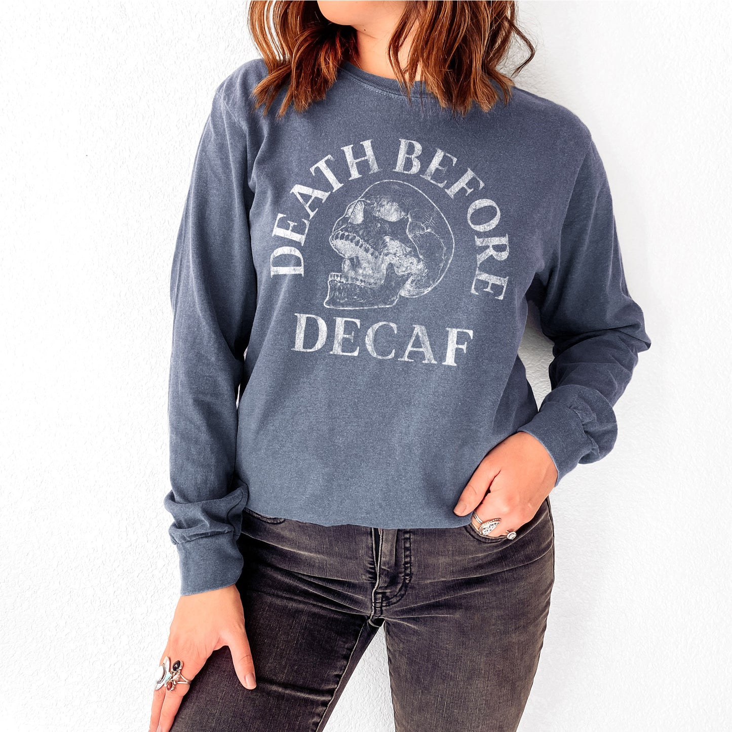 
                  
                    a young woman wearing a long sleeve death before decaf skull shirt in denim
                  
                