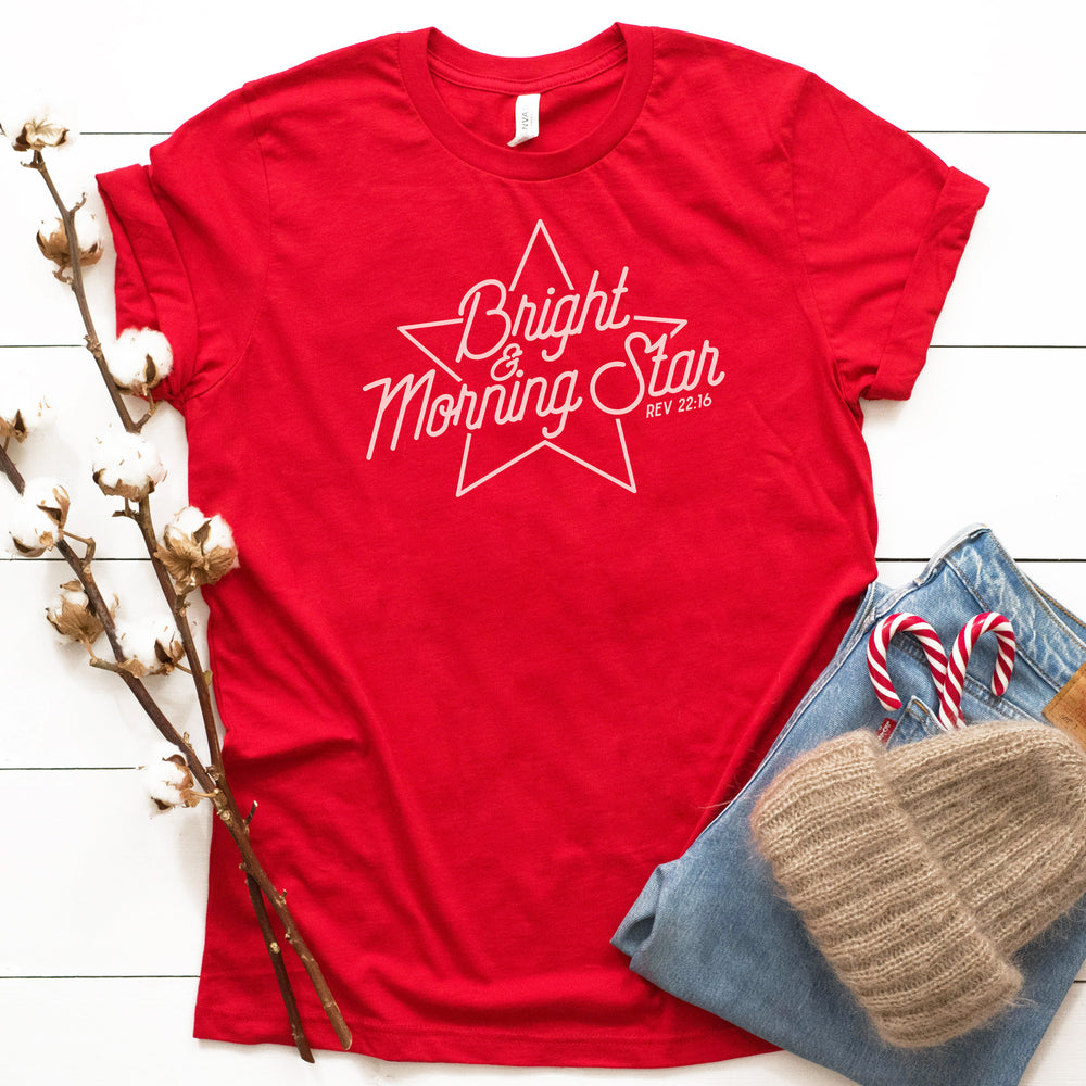 
                  
                    bright-morning-star-svg in white on a red tee, layed out with jeans, candy canes and a cozy beannie
                  
                