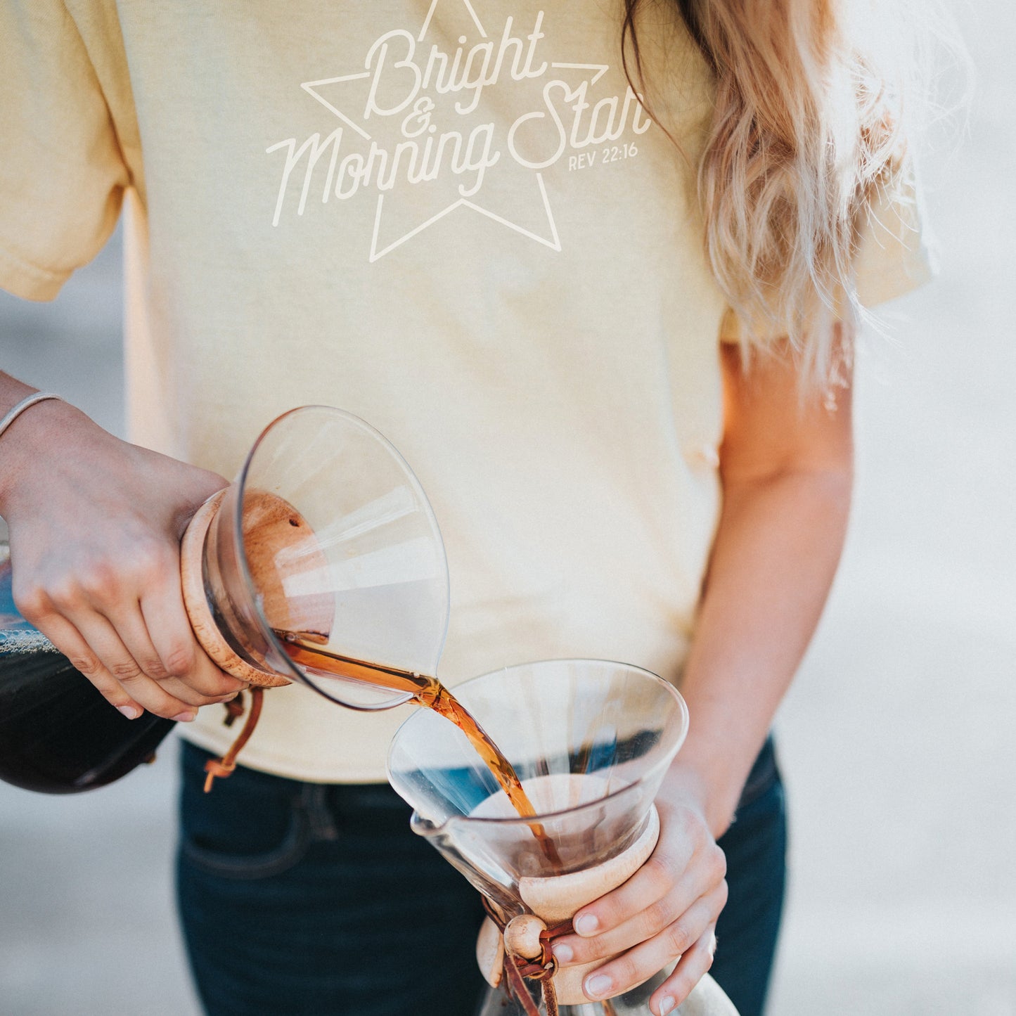 
                  
                    a young woman pouring coffee outside, wearing a yellow shirt with bright-morning-star-svg in white
                  
                
