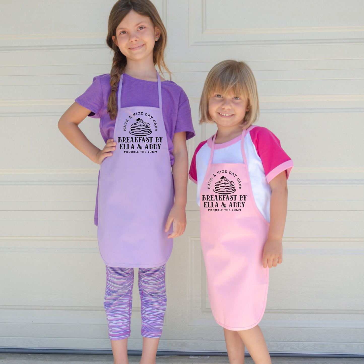 
                  
                    two little girls wearing personalized pancake aprons in pink pastel and purple
                  
                